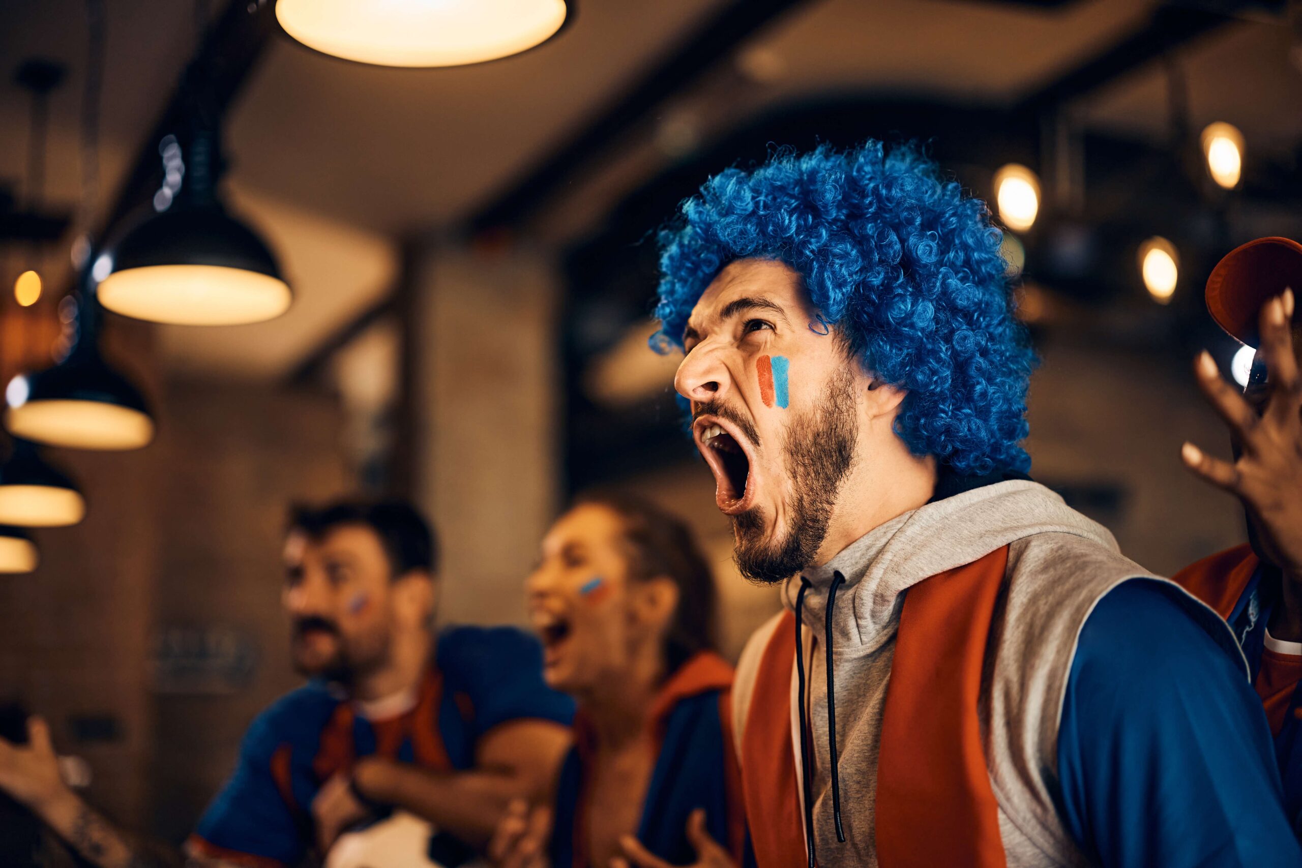 Passionate soccer fan cheering for his team while watching game with friends in pub.